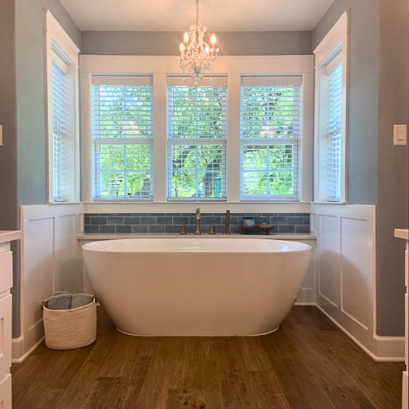 Warm toned hardwood in a farmhouse bathroom with a free-standing tub and blue subway tile.