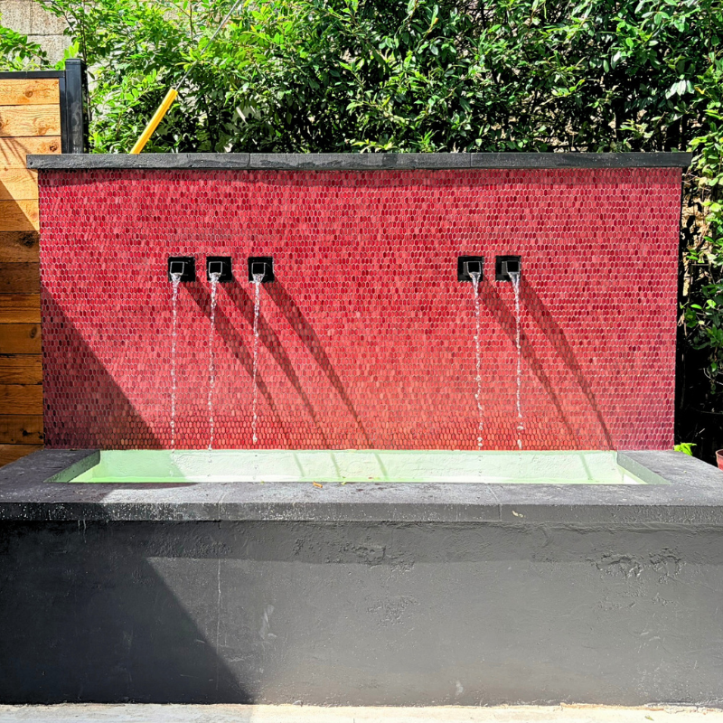Glossy, red tile on an outdoor fountain in an outdoor dining space.