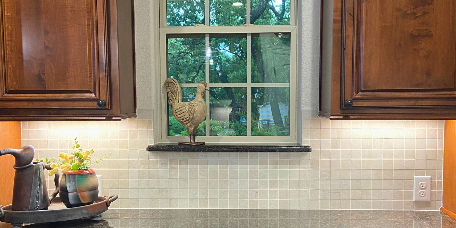 Dark wood cabinets frame a window in a kitchen with a warm white tile backsplash and farmhouse decor.
